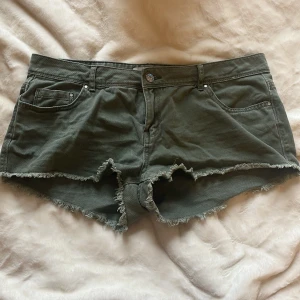 Olivgröna jeansshorts med fransar - Snygga olivgröna shorts i jeansmaterial med råa franskantade benslut. Klassisk femficksmodell med knapp och dragkedja framtill. Perfekta för varma dagar och enkel att matcha med olika toppar. Säljer inte lägre än 150, köpte för 250kr