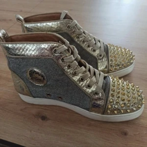 Guldglittriga sneakers med nitar - Säljer ett par unika sneakers i guld med glittriga sidor och ormskinnsmönstrade detaljer. Skorna har snörning och är dekorerade med guldnitar på tån. Perfekta för dig som vill sticka ut med din stil!