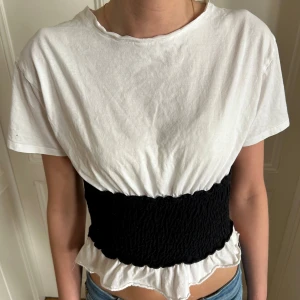 Vit och svart croppad topp - Säljer en trendig croppad topp i vitt och svart. Toppen har korta ärmar, en tight passform över midjan med svart ”korsett” del. Från Zara och är i storlek M men passar XS-M