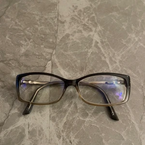 Snygga läsglasögon med Swarovskikristaller - •Läsglasögon med elegant, rektangulär form. •Styrka +1.5 som går såklart att byta och Blue blockers(skydd mot Tv-skärmar och telefoner).  •Bågarna är i grå/brun färg med detaljer i silver och utsmyckade med Swarovskikristaller vid tinningarna. •Mycket fint skick förutom några repor på glaset pga. användning •Märke: Efva Attling