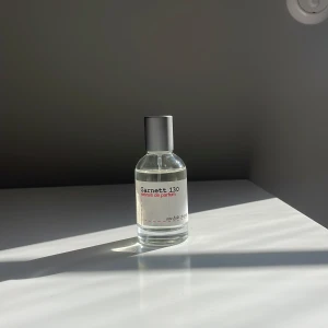 Garrett 130 Eau de Parfum - En stilren parfymflaska i glas med silverfärgat lock. Flaskan är genomskinlig och etiketten är vit med röd och svart text. Parfymen är unisex och har en minimalistisk design som passar perfekt på hyllan.