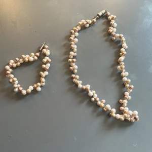 Pärlset halsband och armband i guld- och champagnefärg - Säljer ett matchande set med halsband och armband av glansiga pärlor i guld- och champagnefärg som jag själv har pärlat. Båda har ett tvinnat mönster och magnetlås i silverfärg. Armbandet är 20cm.