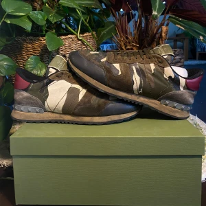 Valentino Rockrunner Camoflage Sneakers - Säljer ett par Valentino Rockrunner sneakers med camouflage-mönster i grönt, beige och brunt. Skorna har detaljer i mocka och skinn samt en röd hälkappa. Klassisk rund tå och snörning framtill. Välanvända med defekter men i dugligt skick. Storlek 43 och true to size. Nypris 8000kr. Fler bilder finns i DM! 