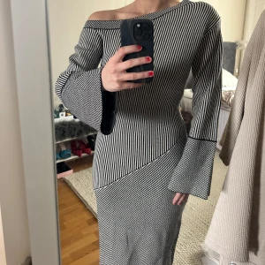 Adoore klänning - Ny med prislapp! Modellen heter Bolzano dress. Svartvit långklänning med smala ränder och asymmetrisk offshoulder-skärning. Klänningen har vida långa ärmar och figurnära passform som framhäver siluetten. 
