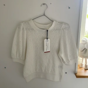 Vit topp med puffärmar från Lindex - Säljer en söt vit topp från Lindex med korta puffärmar och diskret strukturmönster. Tröjan har rund halsringning och ribbade muddar vid ärmslut och nederkant. Perfekt för vår och sommar! Inge defekter! Ny med prislapp. Ordinarie pris 300kr