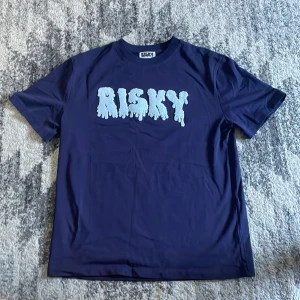 Risky T-shirt  - Snygg mörkblå t-shirt från Risky med ett stort, vitt tryck på bröstet. Storlek L bara använd en gång och tvättad. Pris kan diskuteras