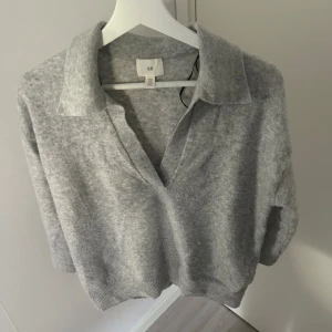 Grå stickad tröja från H&M - Mysig grå stickad trekvartsärmad tröja från H&M med v-ringning och krage. Tröjan har kortare ärmar och en avslappnad passform, perfekt för lager-på-lager. Enkel och stilren design som passar till mycket! 💗