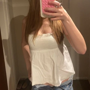 Vit ärmlös linnetopp - Säljer en söt vit ärmlös linnetopp med smock upptill och lös passform nedtill. Perfekt för varma dagar och enkel att matcha med jeans eller shorts.