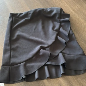 Svart volangkjol från NLY ONE - En kort omlottkjol från Nelly i stretchiga material. Den är kort på mig som är 160 cm. 