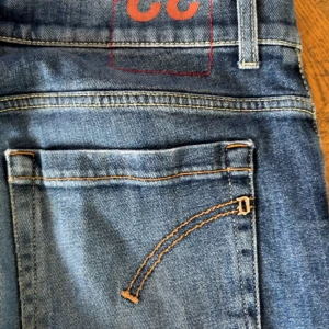 Blå jeansbyxor från Dondup - Säljer ett par klassiska blå jeansbyxor från Dondup med raka ben och snygga detaljer på bakfickorna. Jeansen har normal passform och är tillverkade i ett slitstarkt denimtyg. Perfekta för dig som gillar stilrena och tidlösa jeans.