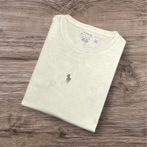 Ralph Lauren T-shirt – Beige (Passar ca 170 cm)  - Ralph Lauren T-shirt – Beige (Passar ca 170cm) 🤍  Säljer en stilren beige Ralph Lauren t-shirt i toppskick! Perfekt till både vardag och avslappnade tillfällen – klassisk design och bekväm passform 🐎 	•	Färg: Beige 	•	Storlek: Passar dig som är ca 170 cm lång (se mått nedan) 	•	Mått: 📏 Längd 65 cm, armhåla till armhåla 45 cm, axel till axel 40 cm 	•	Nypris: ca 1800 kr 💸 	•	Skick: Billigt pris på grund av defekt på sista bilderna – syns knappt när t-shirten används ✅ 109