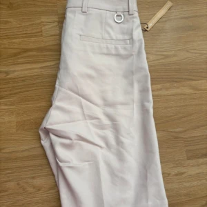 Beiga kostymshorts från STOCKH LM - Snygga ljusrosa kostymshorts från STOCKH LM. Shortsen har hällor för bälte, dekorativ metallring och fickor bak. Nya med prislapp 