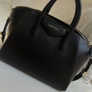 Svart handväska från Givenchy - Väskan är perfekt för att bära både i handen och över axeln med hjälp av förlängd rem, Klassisk design med Givenchy-logga framtill. Några tecken på slitage se bilderna annars inga tecken på användning. Köpt på en vintage secondhand affär i Köpenhamn för några år sedan. Priset pga slitage på gulddetaljerna 