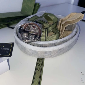 Gucci bälte med silverfärgat spänne - Säljer ett stilrent Gucci bälte i ljusgrått tyg med klassiskt GG-mönster och ett stort silverfärgat spänne som jag fick i present, säljer pga att den är för liten för mig. Bältet levereras med originalförpackning, dustbag och grönt band med Gucci-logga.                                                               Pris går att diskuteras 