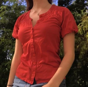 Topp/ Blus - Röd topp med fina knappar, använd några få gånger. Möts på Söder eller Hägersten eller så står köparen för frakt!