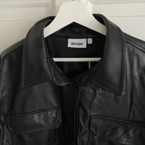 LÄDERJACKA - Jacka/ tröja i läderimitation från Weekday. Aldrig använd och prislapp finns kvar. Nypris: 500 kr. Ena knappen är halv men går lika bra att knäppa med. Möts på Södermalm och vid frakt står köparen för kostnad!