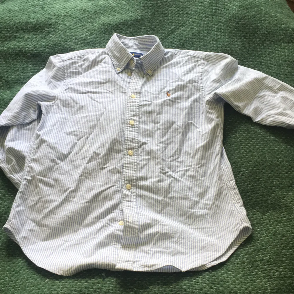 En klassisk ljusblå och vitrandiga Ralph lauren skjort, något figursydd. Storleken small petit. Knappt använd! Säljer för 150kr + frakt! . Blusar.