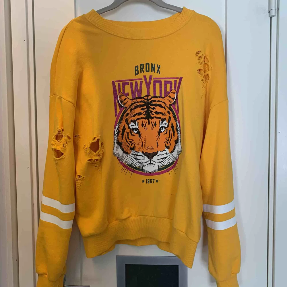 En gul sweatshirt från Gina. Ett tiger tryck på framsidan och vita ränder på armarna. Flera hål och slitna detaljer! Använd ett fåtal gånger. Stl S men passar XS-M beroende på önskad passform. 50kr+frakt. Tröjor & Koftor.