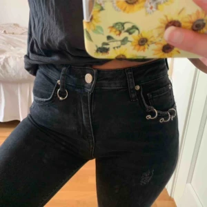  - Svarta/mörkgråa jeans i en tightare passform ursprungligen från Gina Tricot. Silverdetaljer i form av ringar både vid framfickor och vid fotändan, även slitningar vid fotändan. Superbra skick. 
