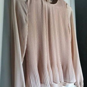 Puderrosa blus från ZARA - Puderrosa blus med volang nedtill och små knäppen i ärmarna respektive nacken. Storlek XS, men passar även S. Sparsamt använd.