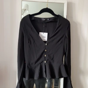 V-ringad blus - En v-ringad blus med knappar i fram, volanger längst ner på blusen och vid ärmarna. Har aldrig använt. Frakt ingår 