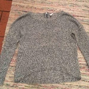  - Grå stickad tröja med en dragkedja vid nacken. Den är kortare fram och längre i bak. Mycket fin i skick. 