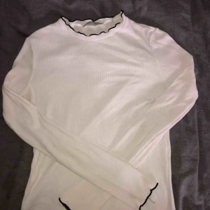  - Vit ribbad långärmad T-Shirt med svarta volanger i kragen och slutet av ärmarna. Köpt på Zara. 