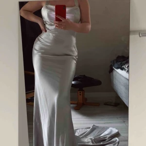  - Silvrig balklänning med släp, aldrig använd. Ca M/L lite oklart då det inte står någon storlek i klänningen. Köpt för 1700 kr på Lizandliz.com. Frakt på 58 kr tillkommer.