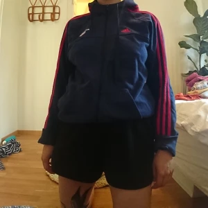 Adidashoodie  - Mörkblå Adidashoodie med röda ränder. Iprincip oanvänd så i gott skick. Jag på bilden är 165 lång och har vanligen storlek s/m
