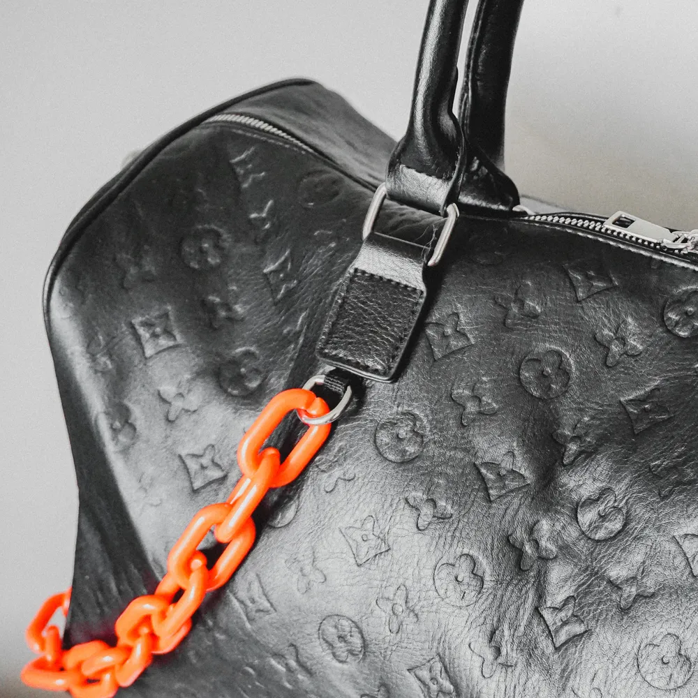 Snygg, stilren väska inspirerad utav Louis Vuitton. Svart med orange plastkedja. Rymmer förvånansvärt mycket, kan användas som ”weekend”-bag. Aldrig använd och har, tyvärr, bara legat i garderoben.. Väskor.