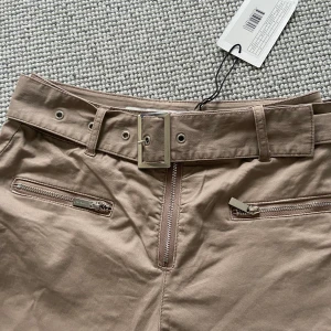 Kostymbyxor beige  - Beigea kostymbyxor med skärp till, silvriga detaljer. Oanvända med prislappen kvar, från ivyrevel.