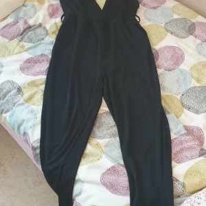 Svart byxdress med öppen rygg - En svart byxdress med öppen rygg och band som du fäster vid nacken. Perfekt för en kväll ute med tjejerna eller en dejt. Funkar också för fester 