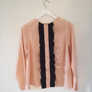  - Blus i färgen nude med volang i svart. Oanvänd.