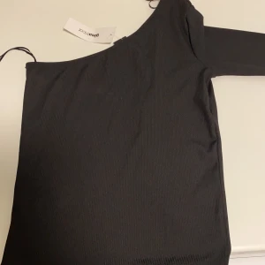 One shoulder topp - En svart fin one shouldertopp. Den är ribbad. Oanvänd, prislappen kvar.