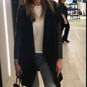  - Svart snygg kappa från Zara med skinnarmar. Något hål på sidan (sömnen som släppt) som inte syns när man knyter med bandet. Man kan även sy in det. Nypris 1300:- 