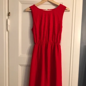  - Fin röd klänning med öppen rygg. Spets upptill, kjolen är längre bak än fram. Kan skicka fler bilder! Färgen på första bilden är mest representativ.  Köpt på Nelly.se för två år sedan, dock aldrig använd.  Frakt betalas av köparen. 