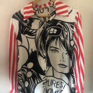 Unik skjorta med comic book-tryck - Häftig skjorta med comic book-motiv och randiga ärmar. Översta knappen som ska sitta vid kragen saknas (bild 3) men annars är skjortan i bra skick. Står att den är 34/36 men är väldigt oversized så passar nog de flesta. Frakt tillkommer! 