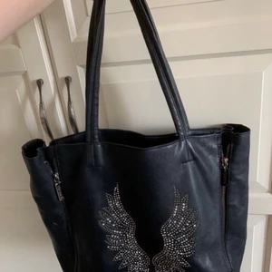 Eternel väska - Svart väska från eternel med vingar på. Väldigt rymlig väska som fortfarande är i bra skick. I väskan får man med en liten necessär som man kan ta av om man vill.