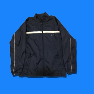 Vintage Nike vindjacka - Vintage marinblå Nike vindjacka.                                     Storlek: S (Pit to pit:51cm).                                              Färg: Vit/Marinblå                                                            Skick: 6/10, märke lite nopprigt + ett litet hål (syns på bilden).                                                                               KÖP NU 250kr. Frakt tillkommer (63kr).                            DM för fler frågor! 