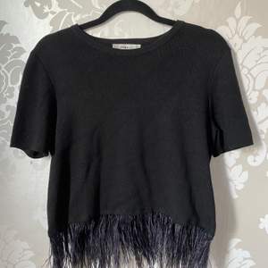 En svart glittrig tröja från Zara med fjädrar längst ner (glittret syns inte mycket när man har den på sig). Materialet är tjockare än vad det är på en vanlig T-shirt. Endast använd 1 gång. Frakt tillkommer.