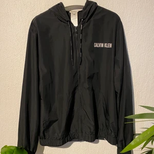 CALVIN KLEIN BLACK WINDJACKET MED LOGGA - CALVIN KLEIN BLACK WINDJACKET WITH LOGO.        Bra skick, knappt använd dock ett litet hål i den. Passform L (True to Size) 