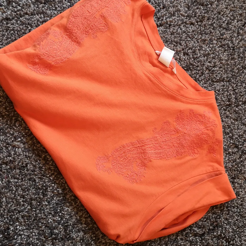 Orange t-shirt med något liknande blom/kurbits mönster på framsidan. . T-shirts.