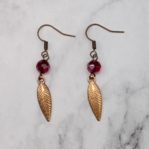  - Bronsfärgade örhängen med glaspärlor och löv/fjäder. Nickelfria. Fri frakt vid köp över 100:-.