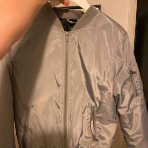  - Tvääärfet bomberjacka i silver. Den e ganska tjock så man blir inte lätt kall. Säljer pga används allt för sällan. Så inte några defekter eller sådant. Köpt på lager för jag vet inte hur mycket.