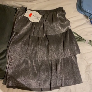 Glittrig Volangkjol från NAKD  - Glittrig volangkjol från Nakd. Köpt för 250kr men säljer för 100kr. Aldrig använd därav prislappar kvar. 