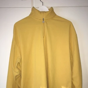  - Gul fleecetröja med polokrage samt detalj på dragkedjan.