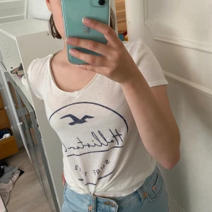 Hollister T-shirt - Fin vit Hollister T-shirt med blått tryck! Den är i storlek XS men passar en S också. Den är i fint skick, använd fåtal gånger! Vi kan diskutera hur vi gör med frakten annars kan den hämtas i Sundsvall 📍 🧚🏼