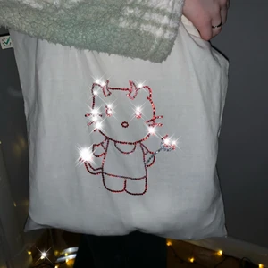 Tygkasse evil hello kitty - En nostalgisk och riktigt cool tunn tygkasse gjort av 100% ekologisk bomull! Mått: 38x42 cm Det tar flera timmar att göra dessa bling-designer då endast en sten tar ca 25 sek att få fast, därav priset 🥰🦋 Har lagt ner mycket tid och kärlek i detta! 