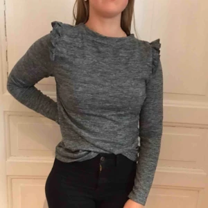  - Fin grå långärmad. Liten volang på axlarna, passar upp till en M