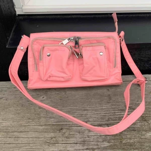  - Börjar om budgivningen! Snygg väska från nunoo i babyrosa färg. Går inte att köpa längre.   Nypris: cirka 1200kr  Bandet går att förkorta och förlänga.   Mått: 25x15 cm   Aldrig använd. LÄGG BUD! Frakt kostar 60kr och jag ansvar ej för postens slarv. 